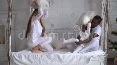 快乐混血家庭妈妈，非洲爸爸和小女儿在床上玩枕头大战。 多民族青年